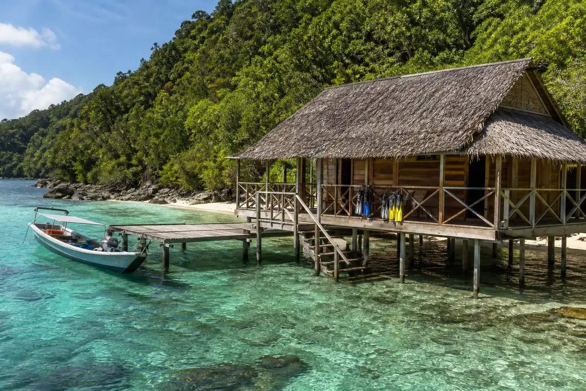 Stilted wooden homestay bungalow and jetty over clear shallow water in Raja Ampat, the land-based alternative to a liveaboard