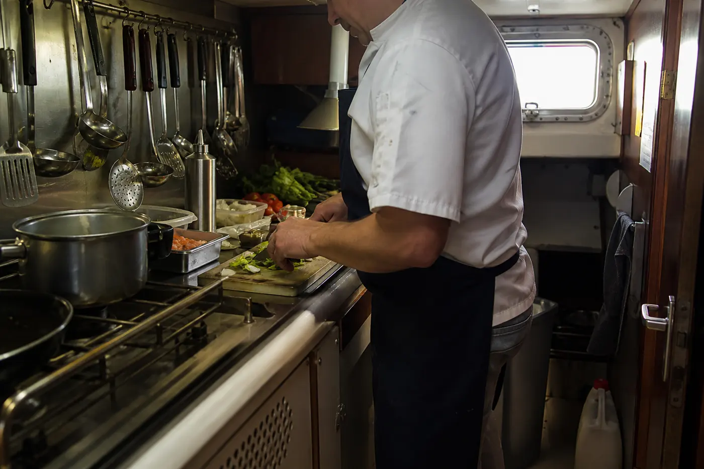 Cook preparing vegetables in a cramped liveaboard galley, showing the limited counter space that makes allergen separation difficult