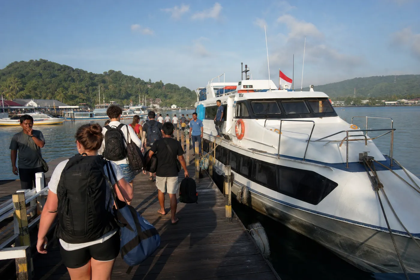 Travellers with backpacks and dive bags boarding the express ferry to Waisai at a tropical Indonesian harbour jetty
