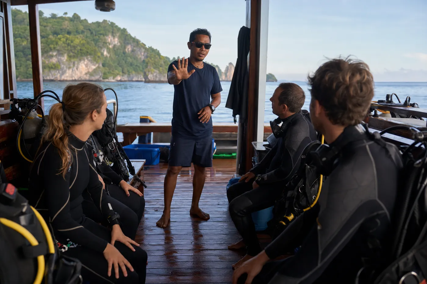 Dive guide demonstrating the stop hand signal to guests during a pre-dive briefing on the deck of an Indonesian liveaboard