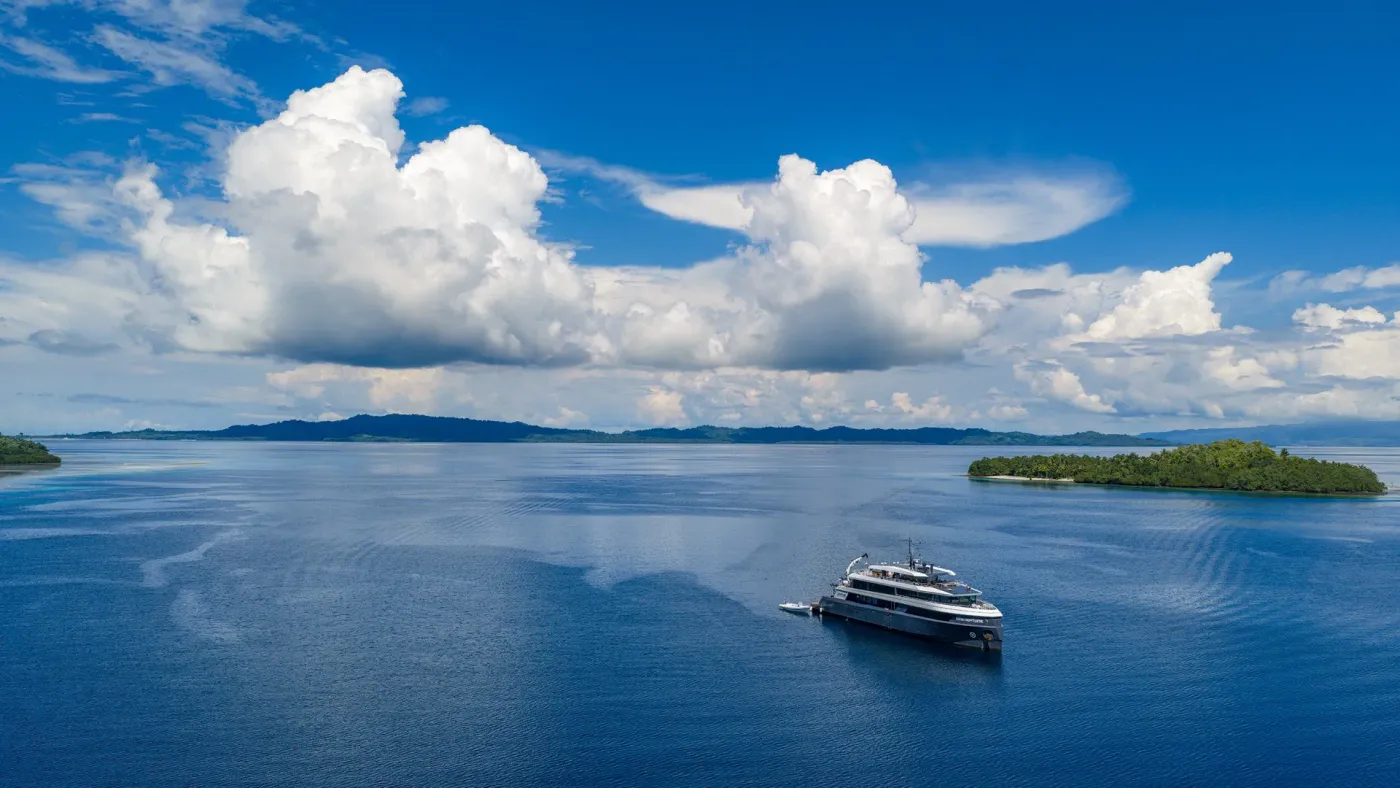 Neptune liveaboard cruising across open sea toward distant islands in Indonesia